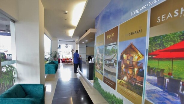 A hotel corridor with teal sofas, a reception desk, and promotional posters for Langkawi and Gemala. - Geopark Hotel, Kuah Langkawi (Langkawi)
