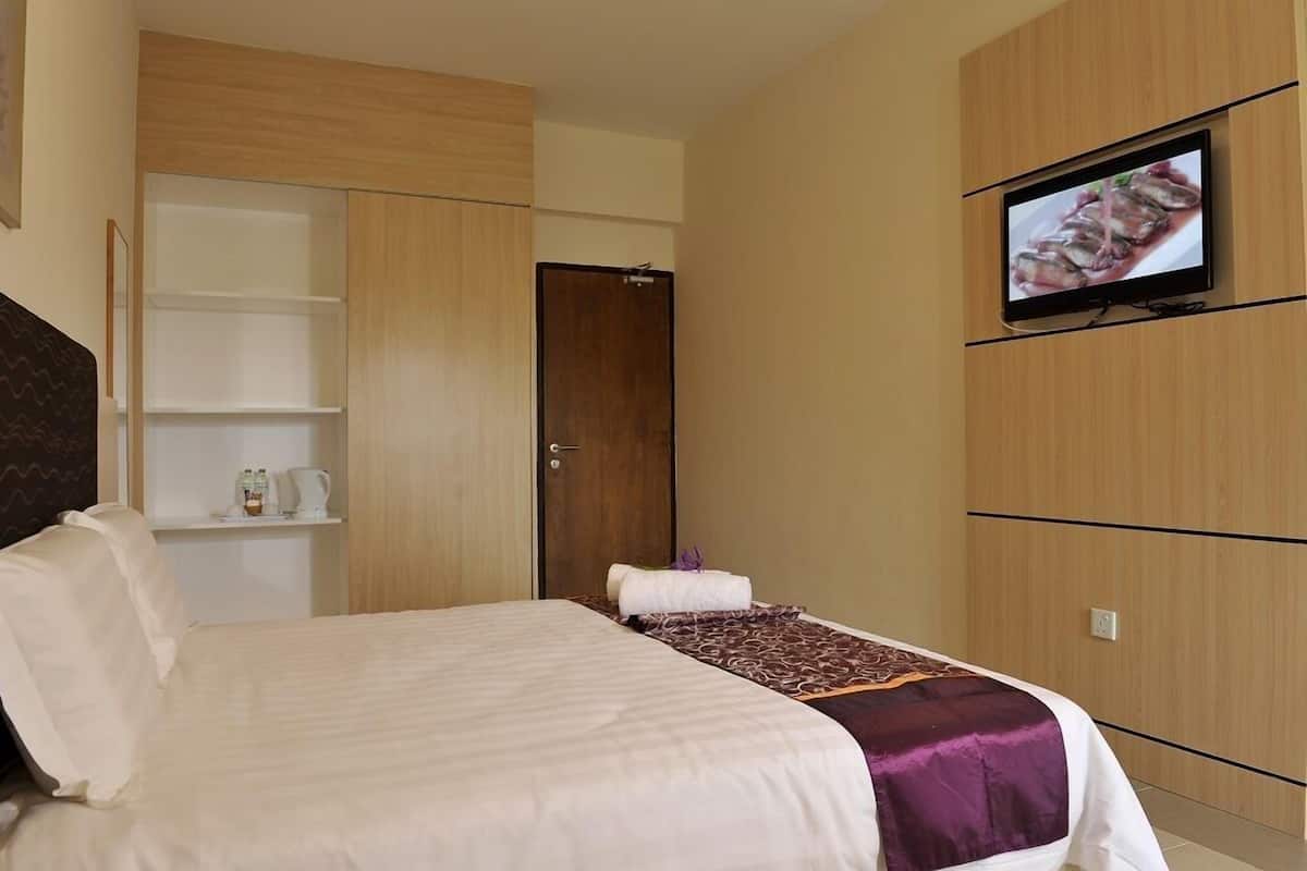 Une chambre d’hôtel avec un lit, un téléviseur fixé au mur et une armoire.