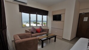 A hotel room with a sofa, armchair, and a bed. There is a window with a view of the sea and palm trees. A flat-screen TV is mounted on the wall. - Geopark Hotel, Kuah Langkawi (Langkawi)