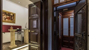 A hotel lobby with a wooden door, a marble column, and a red cushioned bench. - Pantheon Caesar Relais (Rome)