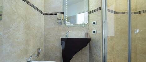 A modern bathroom with a white sink, a black vanity, a glass shower enclosure, and a mirror with lights.