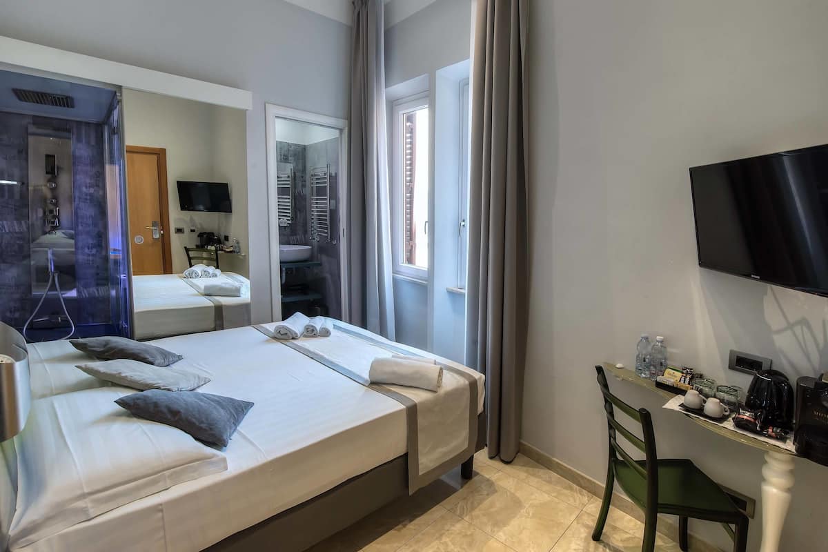 A hotel room with a bed, a desk with toiletries, a TV, and a window with curtains.