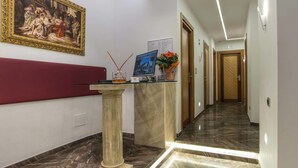 A reception area with a marble reception desk, a framed painting, a computer, and a vase with flowers. - Pantheon Caesar Relais (Rome)