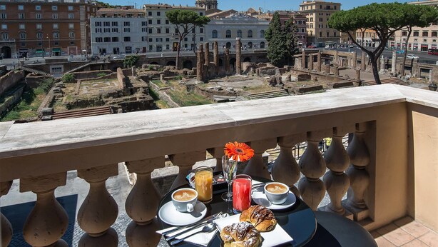 A balcony with a table set for breakfast, overlooking ancient ruins and modern buildings. - Pantheon Caesar Relais (Rome)