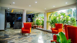 A lobby with red chairs, a reception desk, and a large window with plants. - Fritz Apartments and Suites (Abuja)
