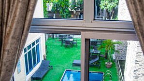 A view of a swimming pool from a window, with a grassy yard and outdoor furniture visible. - Fritz Apartments and Suites (Abuja)