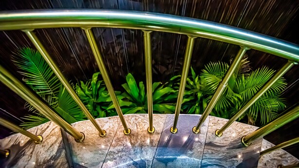 A marble staircase with a golden handrail, surrounded by lush green plants. - Fritz Apartments and Suites (Abuja)
