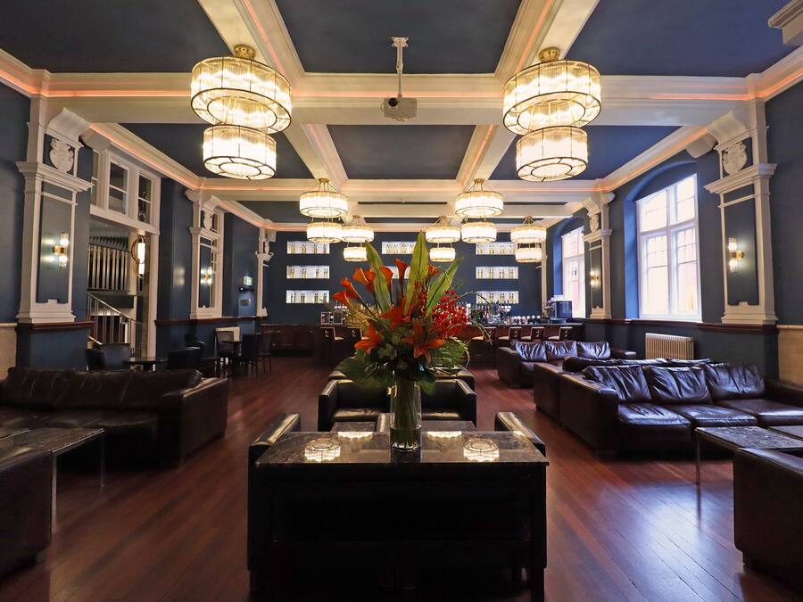 A spacious lobby with dark blue walls, multiple seating areas, and large chandeliers.