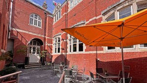 An outdoor patio area with brick walls, tables, chairs, and an orange umbrella. - Morgans Hotel (Swansea)