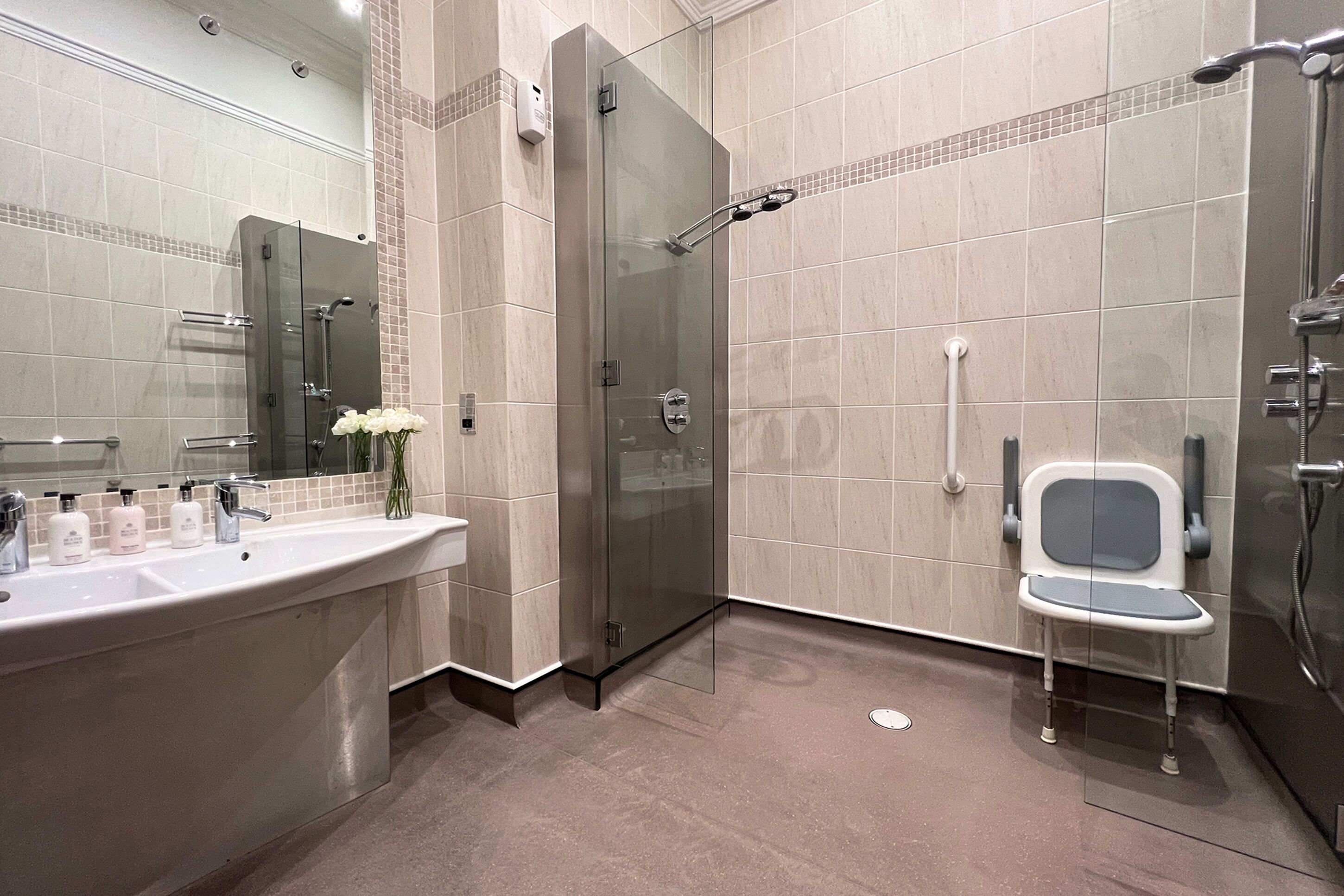 A modern bathroom with a glass-enclosed shower, a vanity with a large sink, and a small chair.