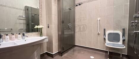 Ein modernes Badezimmer mit einer gläsernen Duschkabine, einem Waschtisch mit großzügigem Becken und einem kleinen Stuhl.