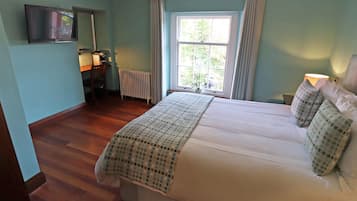 Una camera da letto con un letto, una scrivania, una sedia, un termosifone, una televisione e una finestra con tende.