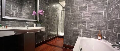 A modern bathroom with a large mirror, a white bathtub, and dark tiled walls.