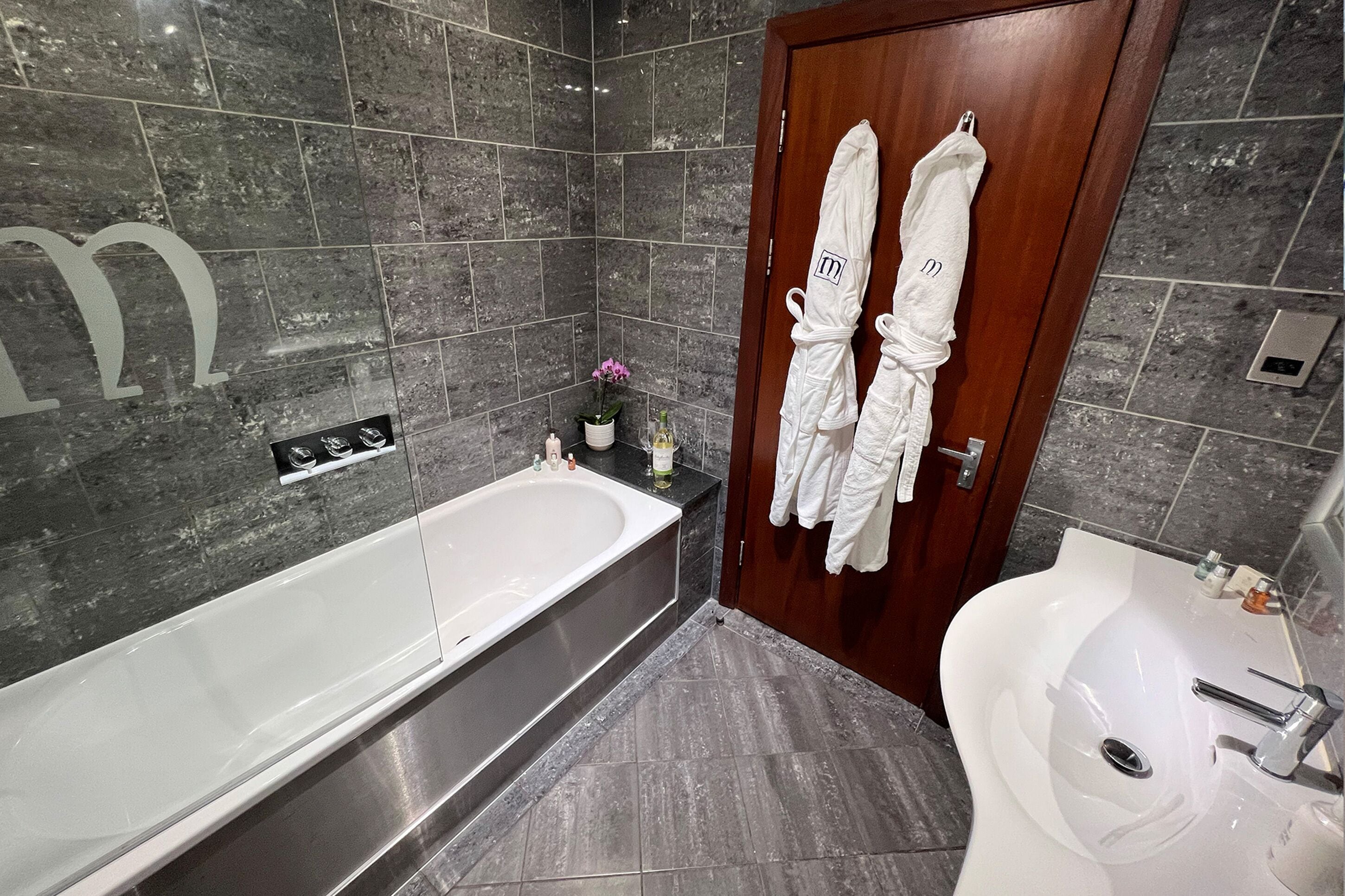 Un baño moderno con una bañera grande, un lavamanos y una ducha. Hay dos toallas blancas colgadas en la puerta.