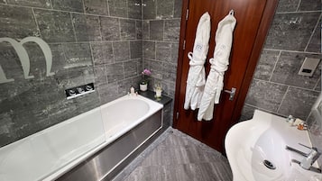 Un baño moderno con una bañera grande, un lavamanos y una ducha. Hay dos toallas blancas colgadas en la puerta.