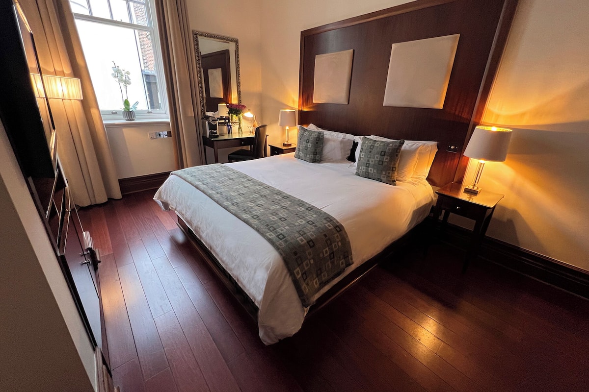 A hotel room with a large bed, bedside tables, a desk, and a mirror.