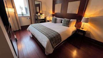 Una habitación de hotel con una cama grande, mesitas de noche, un escritorio y un espejo.