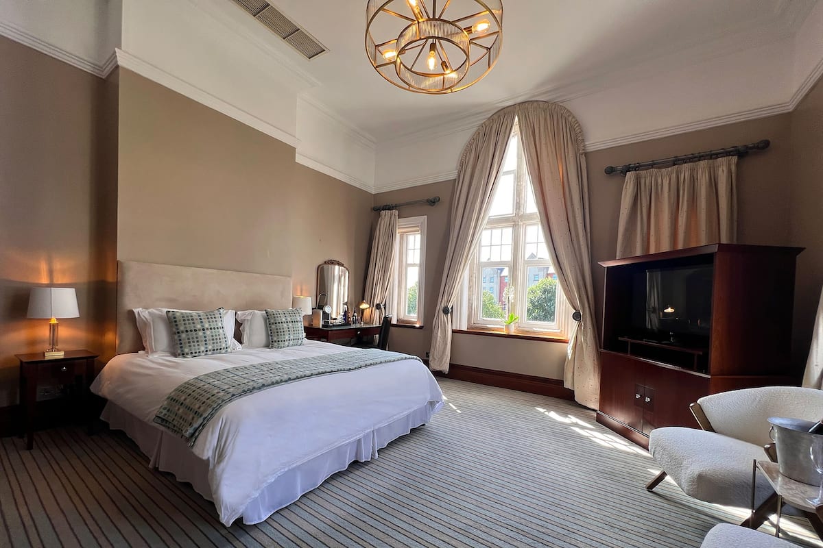 A hotel room with a large bed, a TV, a desk with a lamp, and a chair.