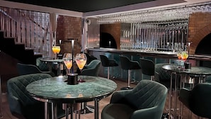 A bar area with round tables, green upholstered chairs, and a brick wall. - Morgans Hotel (Swansea)