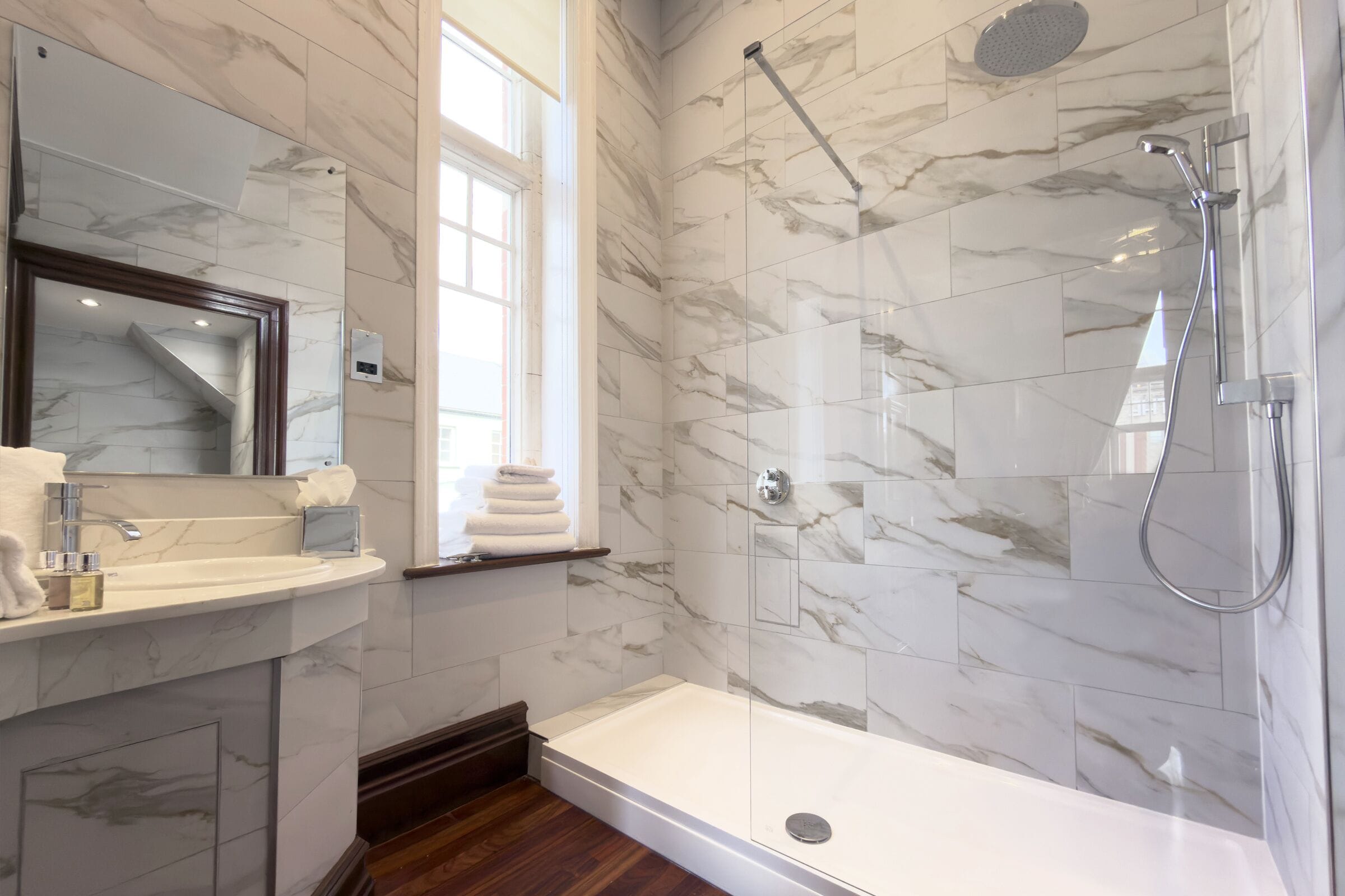 A modern bathroom with a marble-tiled shower, a standalone bathtub, and a vanity with a mirror and towel rack.