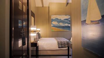 A hotel room with a bed, bedside table, lamp, and a painting of a beach scene.