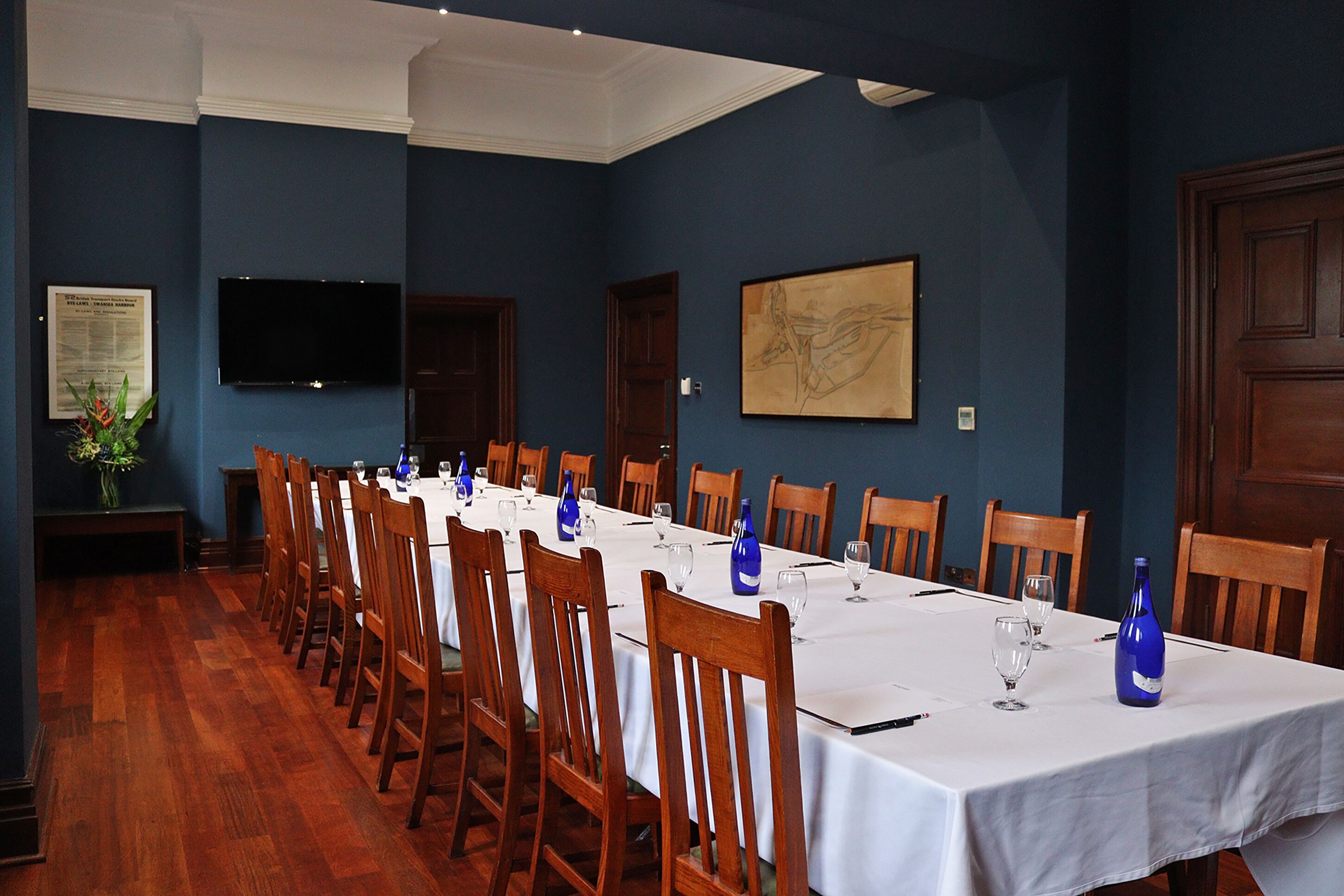 A conference room with a long table, wooden chairs, and a white tablecloth.