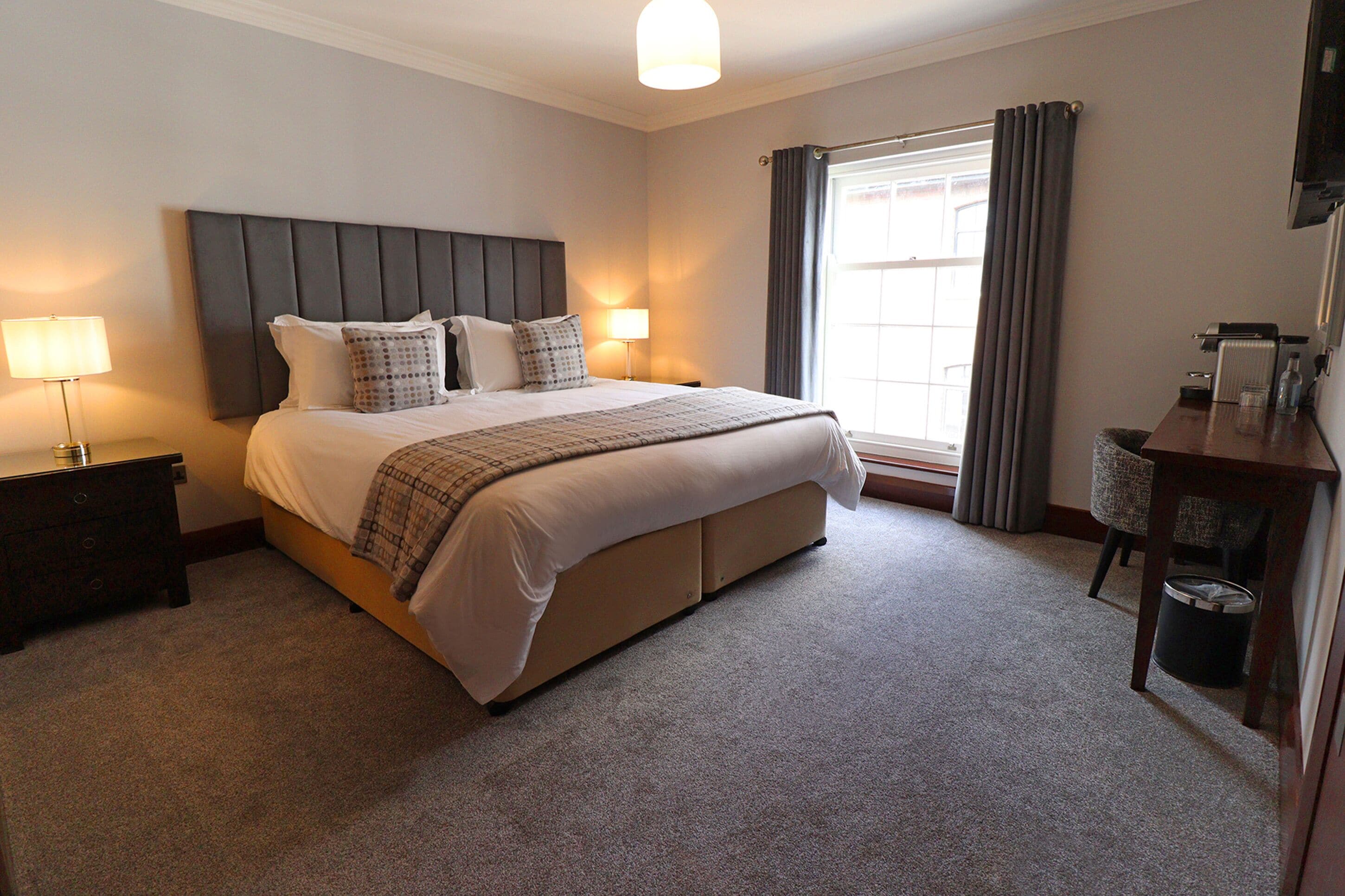 A hotel room with a large bed, bedside lamps, a radiator, a chair, and a window with curtains.