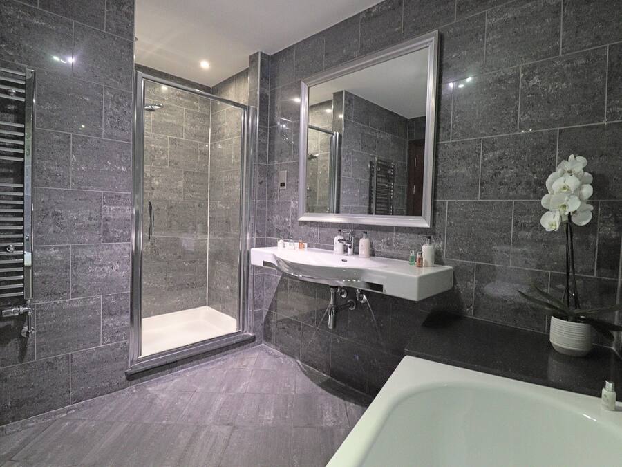 A modern bathroom with a glass shower enclosure, a white sink, and a large mirror.