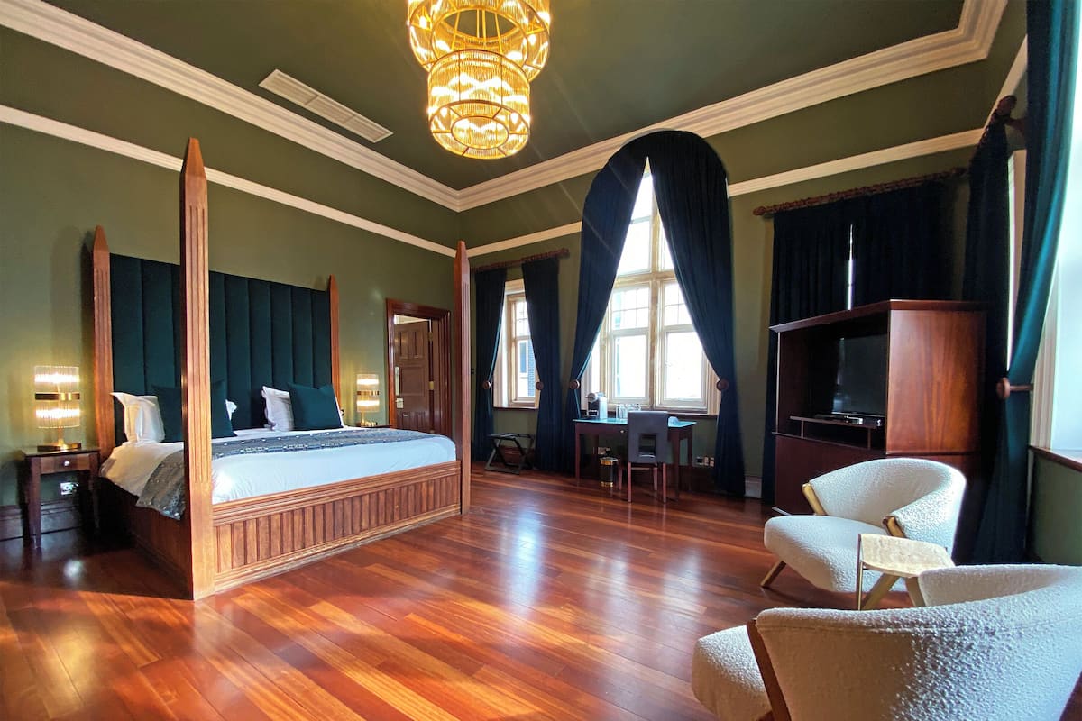 A four-poster bed, a television, a desk, and a chair in a room with wooden flooring and green walls.