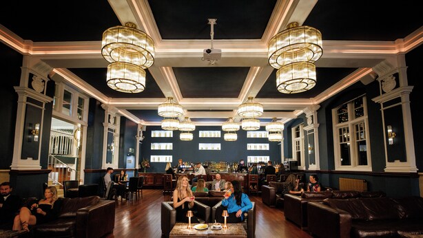 A bar area with multiple seating options, including sofas and tables, and a bar counter with people. - Morgans Hotel (Swansea)