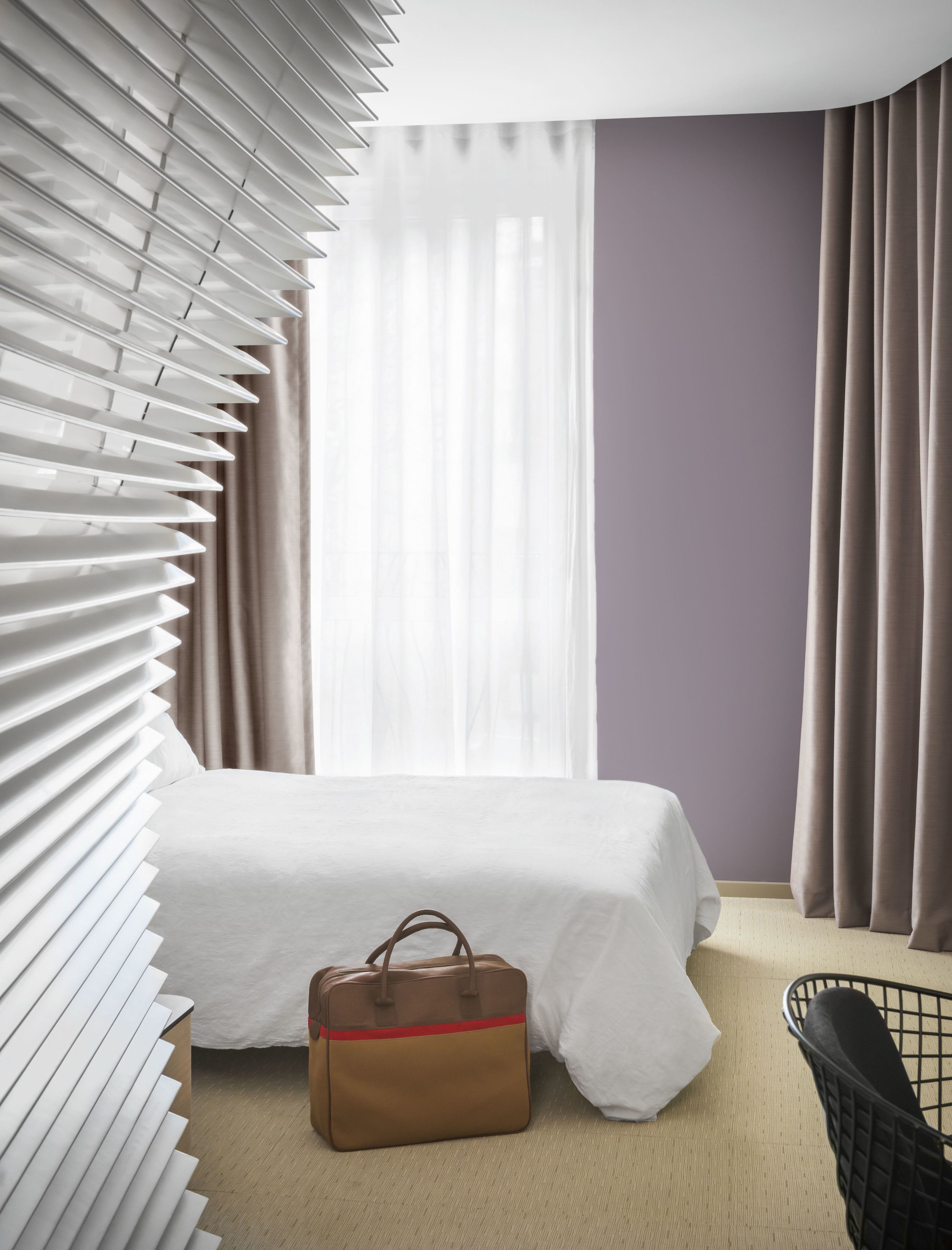 A hotel room with a bed, a suitcase, and a chair.