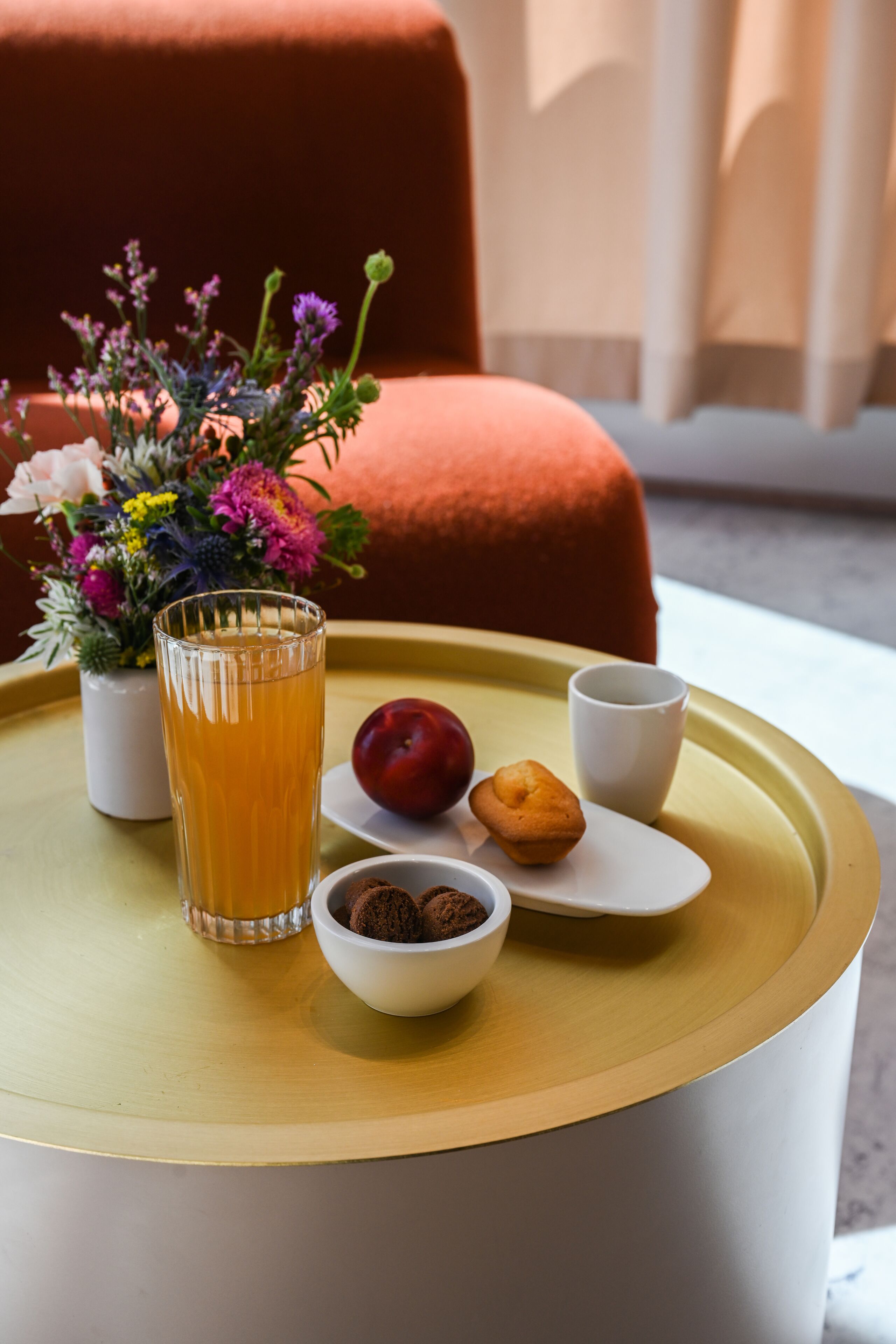A tray with a glass of orange juice, a plum, a muffin, and a bowl of cookies on a round table.
