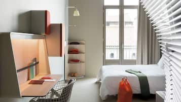 Ein modernes Hotelzimmer mit Bett, Schreibtisch, Stuhl und Blick auf die Stadt durch das Fenster.