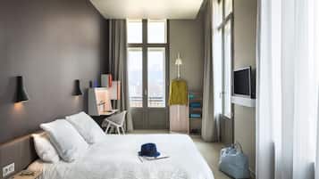 A hotel room with a bed, a desk, a chair, a TV, and a window with curtains.