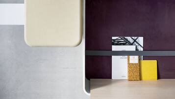 A modern, minimalist room with a grey concrete wall, a white and purple storage unit, and a wooden table.