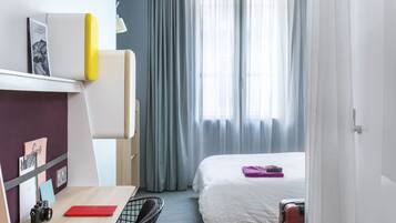 A compact hotel room with a desk, chair, bed, and a suitcase.