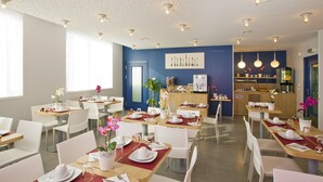 A modern dining area with white chairs, tables set with plates, and a blue accent wall. - Séjours & Affaires Massy Atlantis (Massy)