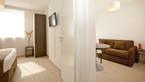 A modern hotel room with a bed, a TV mounted on the wall, a sofa, a small table, and a decorative vase. - Séjours & Affaires Massy Atlantis (Massy)