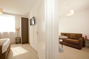 A modern hotel room with a bed, a TV mounted on the wall, a sofa, a small table, and a decorative vase.