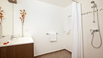 Une salle de bain moderne avec un lavabo blanc, un miroir, une douche équipée d’un pommeau de douche à main et un porte-serviettes.