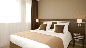 A hotel room with a large bed, white linens, brown pillows, a wooden headboard, a nightstand with a lamp, and a window with sheer curtains. - Séjours & Affaires Massy Atlantis (Massy)