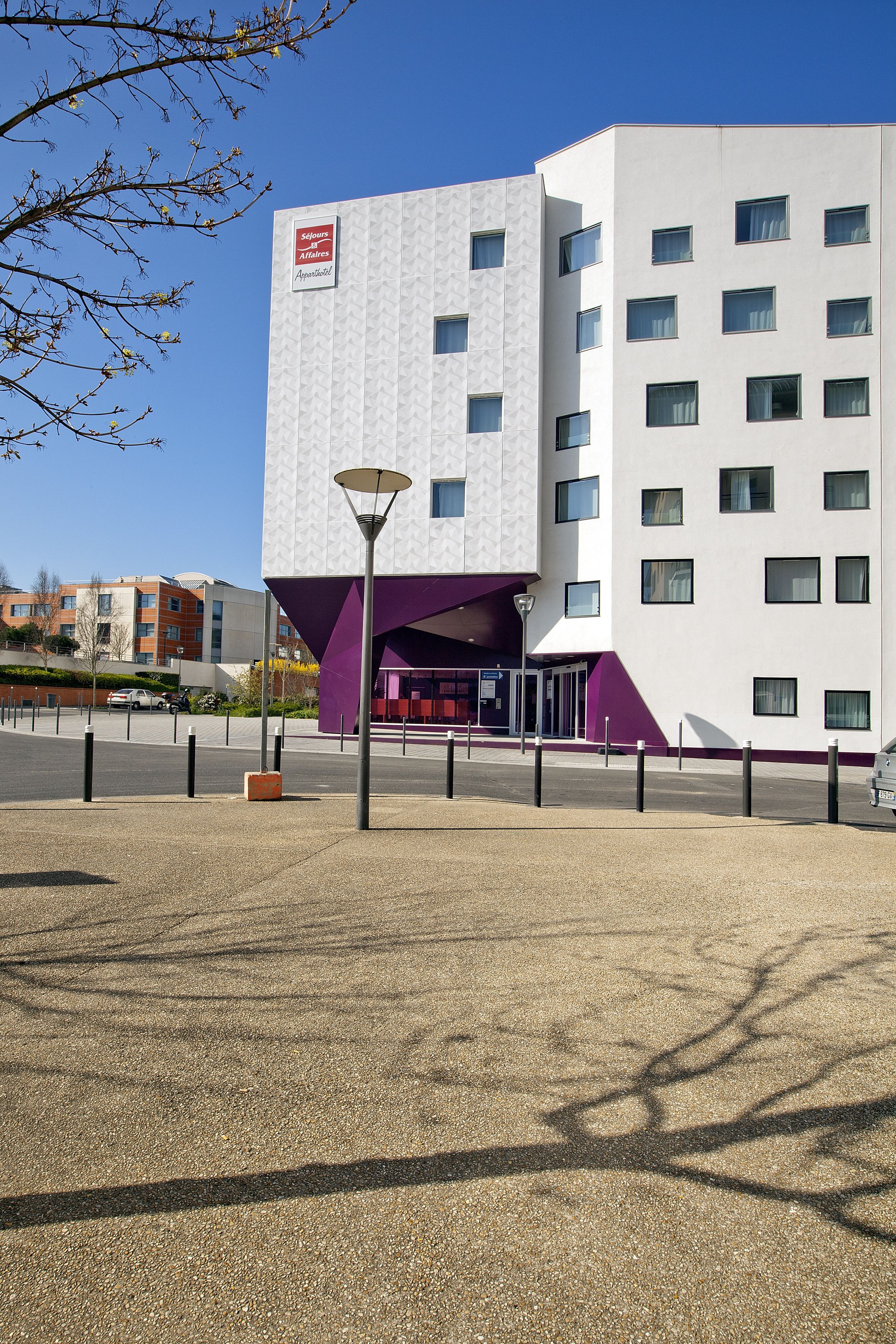 A modern building with a white facade and purple accents, featuring multiple windows and a visible entrance.