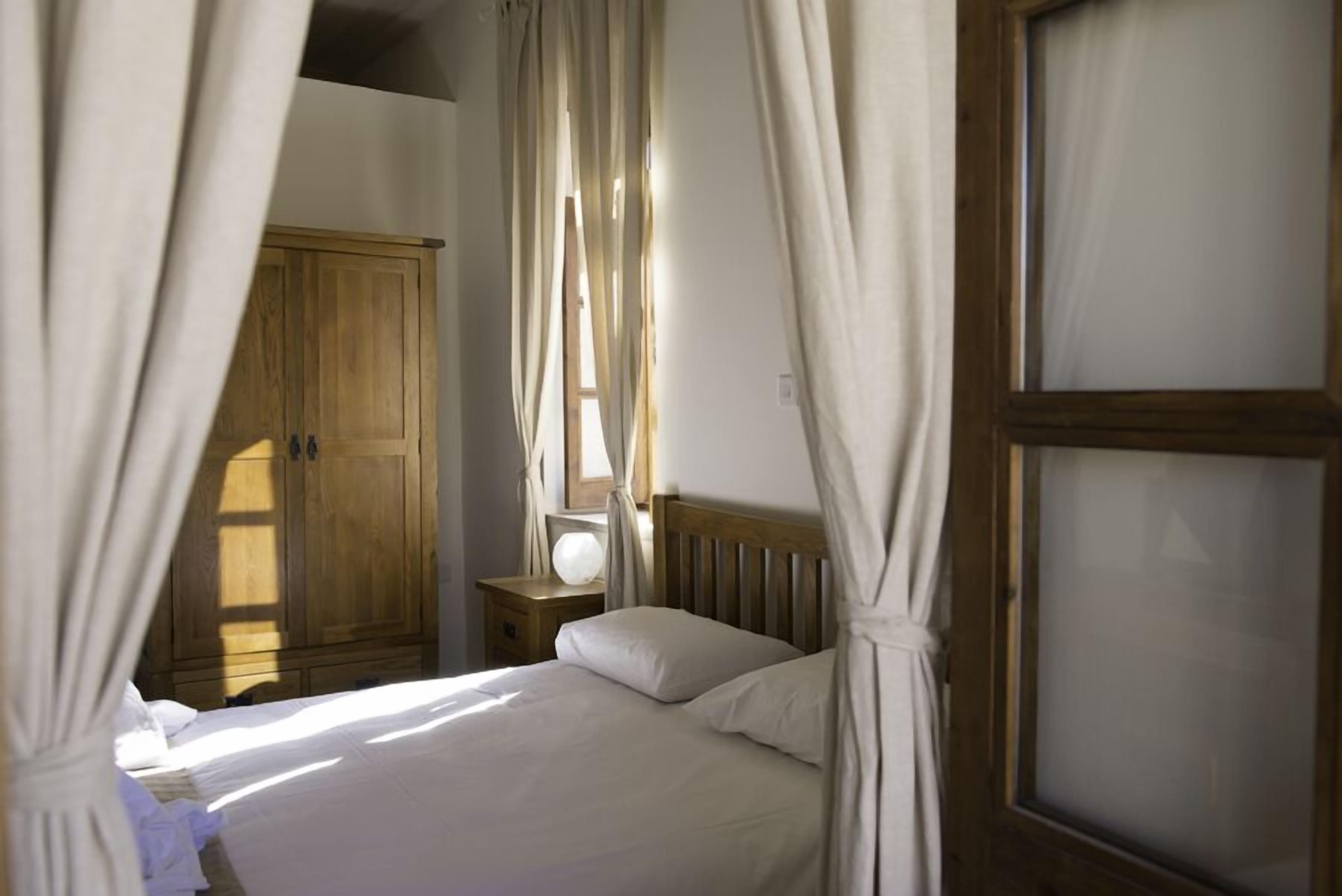 Quarto com guarda-roupa de madeira, mesa de cabeceira com abajur e cama com roupa de cama branca.