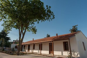 Un bâtiment d’un seul étage, avec un toit recouvert de tuiles, un porche et un vélo garé à l’extérieur.