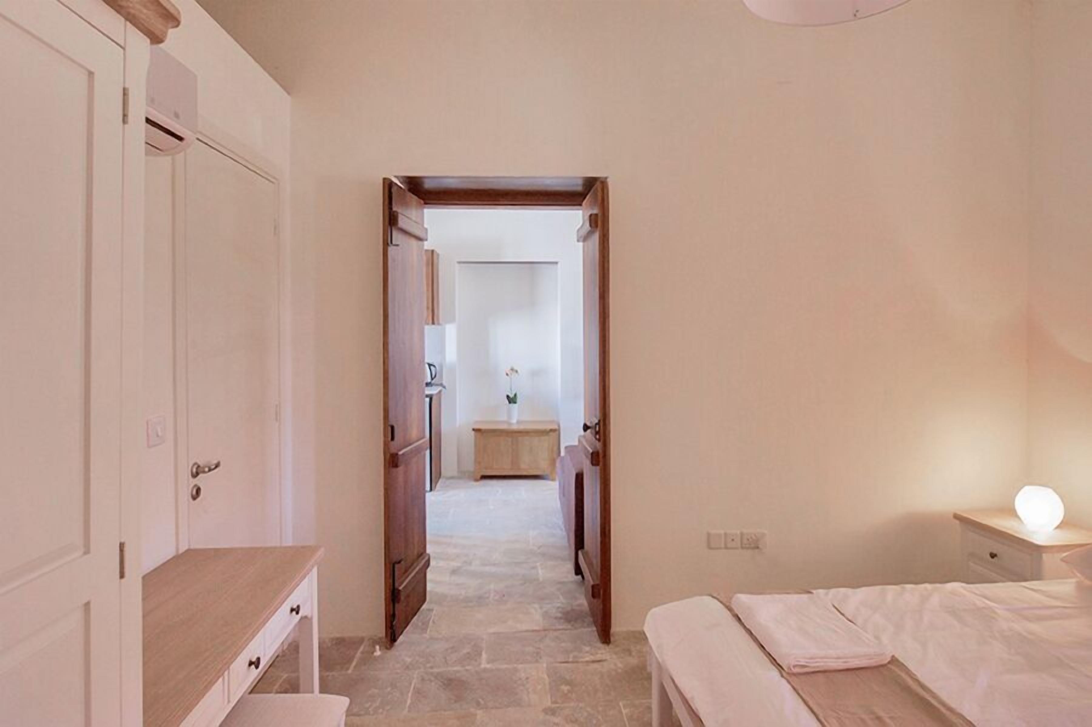 Une chambre à coucher avec un lit, une table de chevet et une petite table avec une lampe. On y trouve également une armoire et un bureau avec des tiroirs.