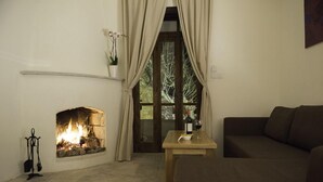 Una sala de estar acogedora con chimenea, un sofá, una mesa con una botella y una copa, y un ventanal con cortinas.