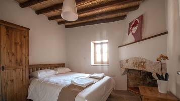 A bedroom with a bed, wooden wardrobe, stone fireplace, and a window.
