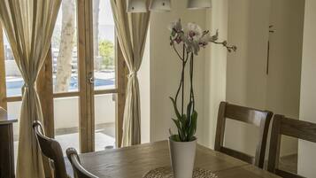 A wooden dining table with a white vase of orchids, wooden chairs, and a woven placemat.