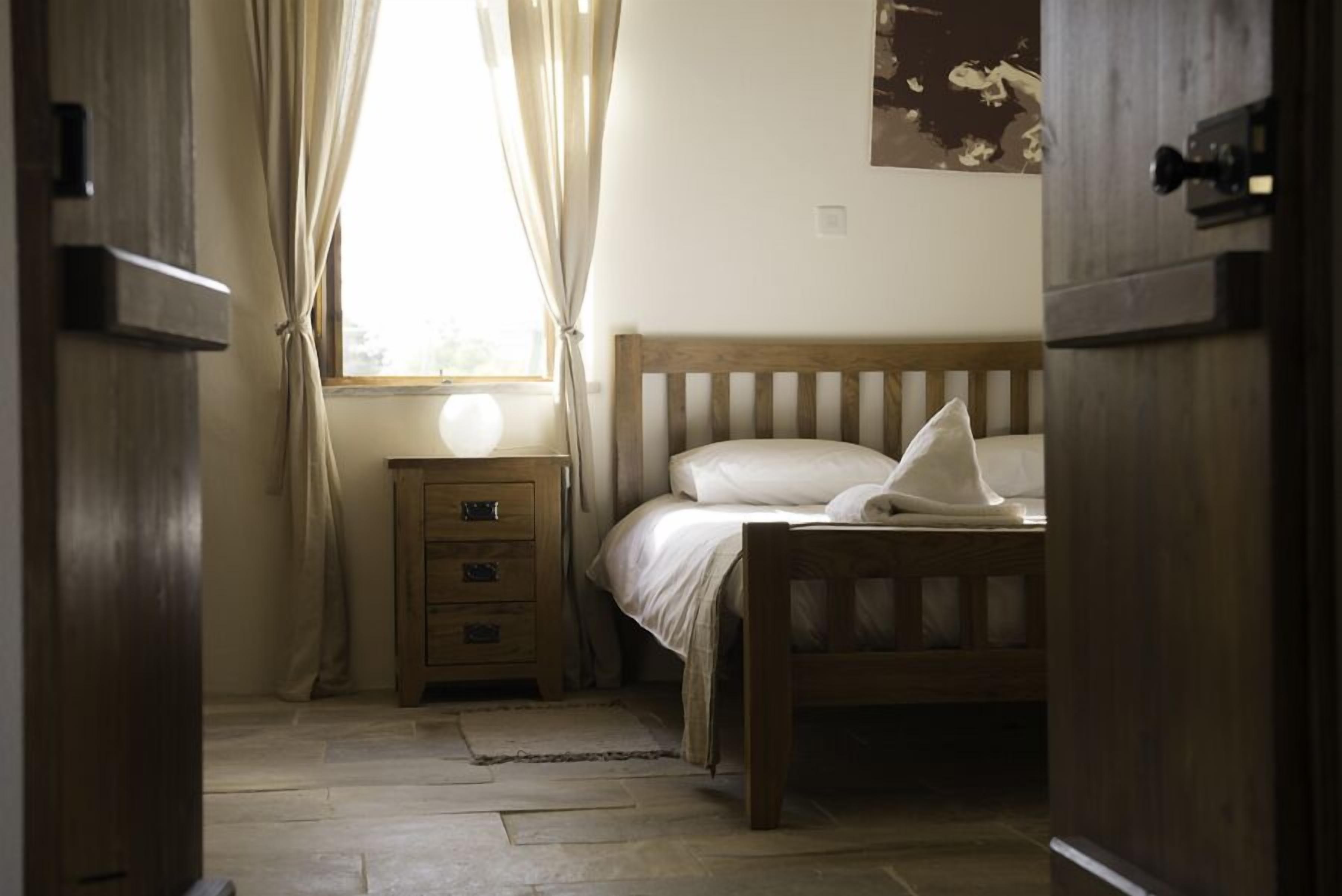 A bedroom with a wooden bed, a nightstand, and a window with curtains.