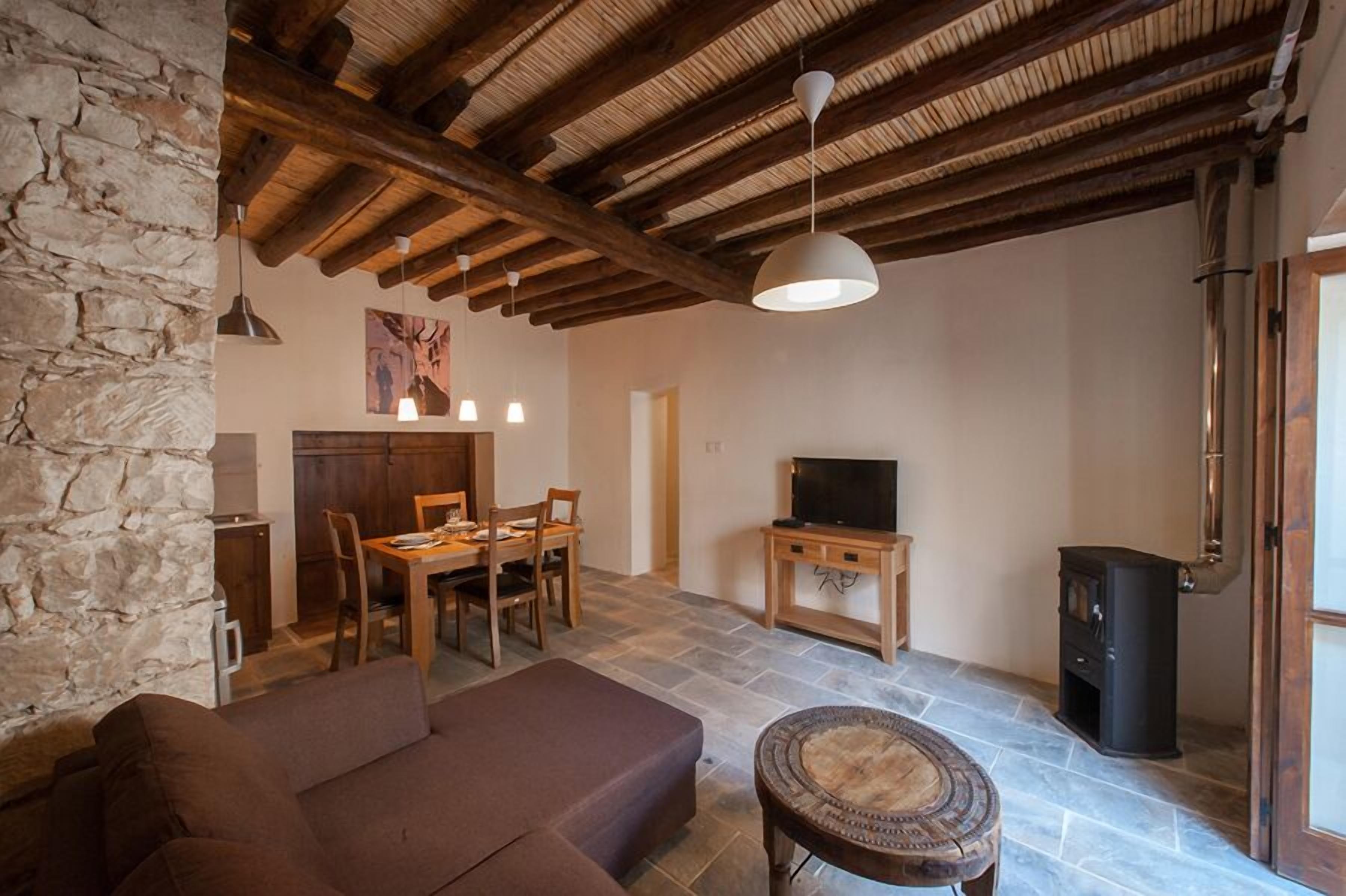 Un salon rustique avec des murs en pierre, un plafond en bois, une cheminée, un téléviseur et un sol en pierre.